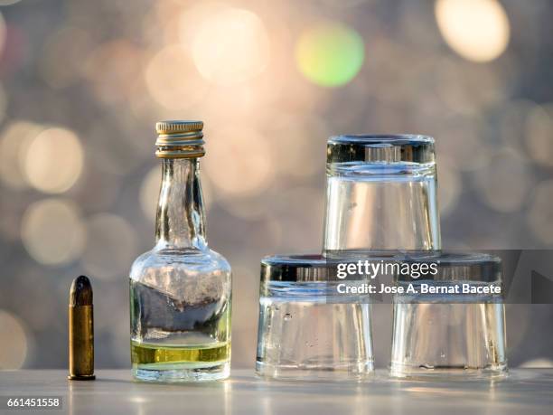 bottle of liqueur and  glasses of chupito close to a bullet , concept of which the alcoholism kills - bebida stockfoto's en -beelden