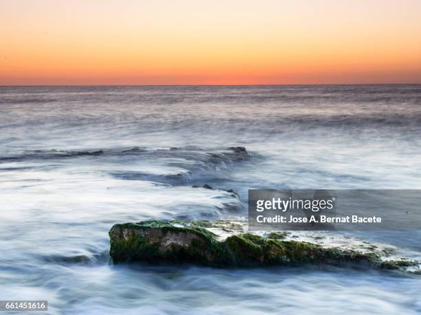 exit of the sun of orange color, on the surface of the sea, in a zone of coast with rocks and waves in movement - luz brillante stock pictures, royalty-free photos & images