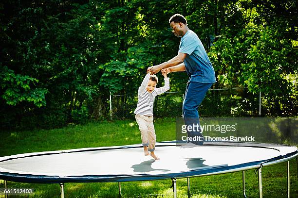 father and son jumping together on trampoline - masculinityundonetrend stock-fotos und bilder