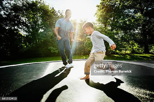 smiling father and young son jumping on trampoline - trampoline photos et images de collection