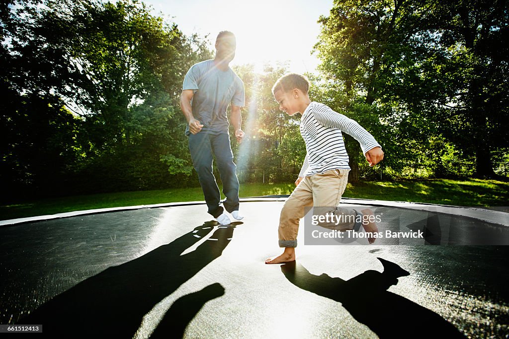 Smiling father and young son jumping on trampoline