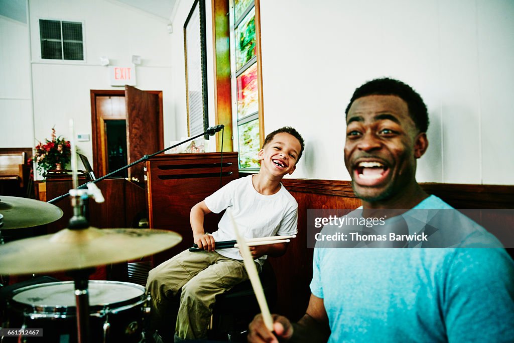 Laughing father and son playing on drum set