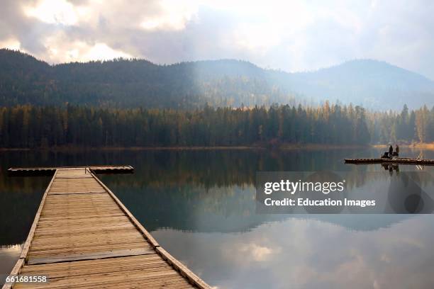 Fishermen on a dock with the reflections and light fog of the calm lake at Round Lake State Park in the panhandle of northern Idaho , Round Lake...