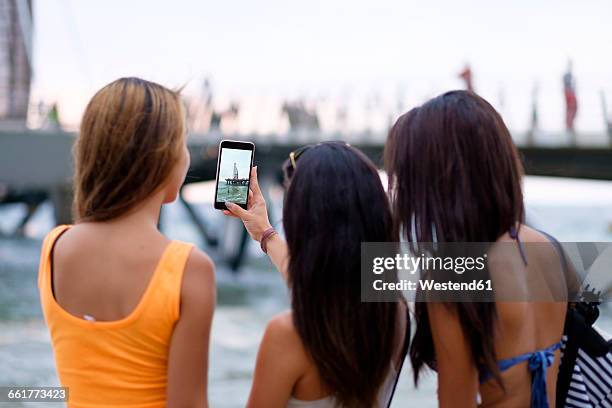 mexico, puerto vallarta, three young women taking a smartphone photo of los muertos pier - dreiviertel rückansicht stock-fotos und bilder