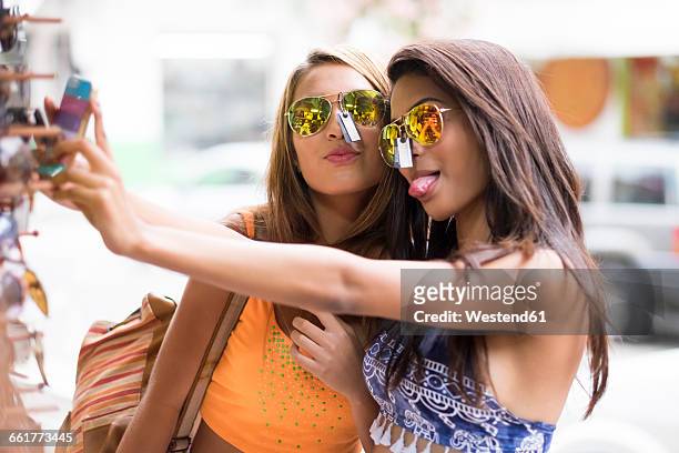 two young women trying sunglasses on and taking a selfie - preisschild stock-fotos und bilder