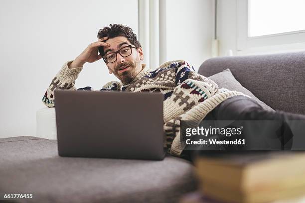 suprised man lying on a couch looking at laptop - young man laptop couch photos et images de collection