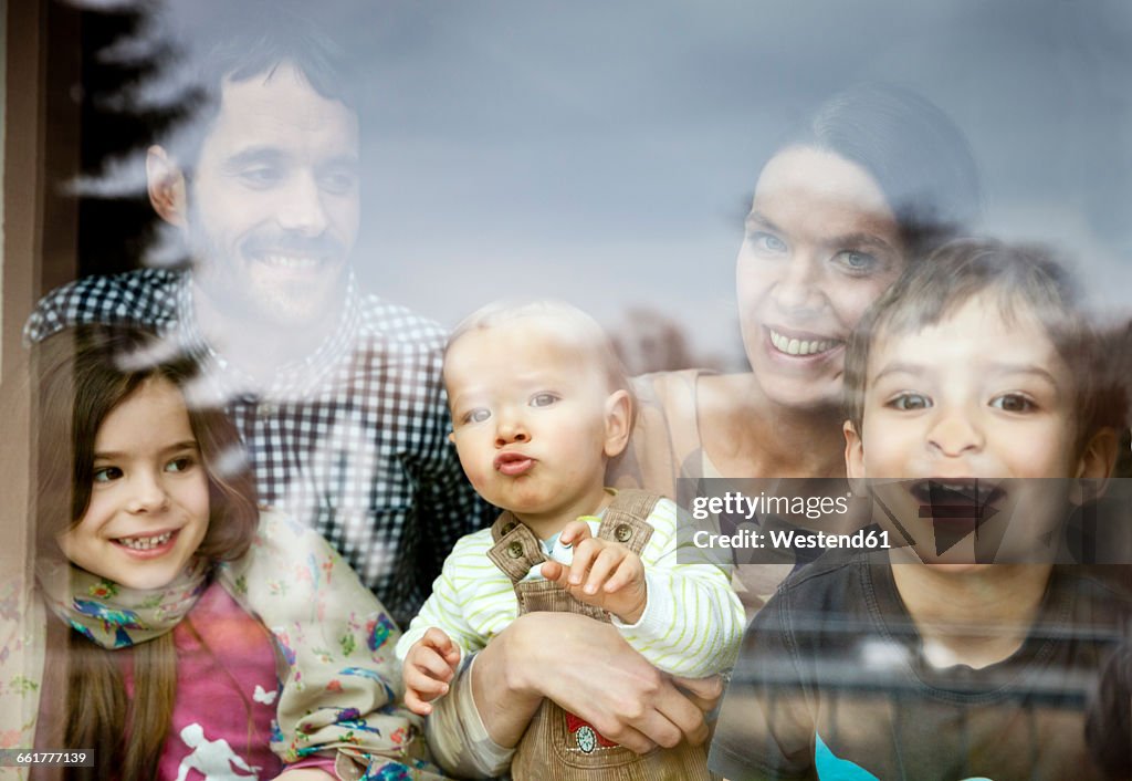 Happy family of five looking through window pane
