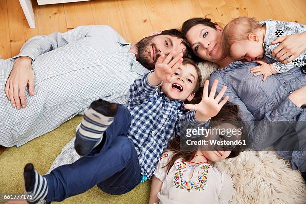 family with three children lying on the floor at home looking at camera - family with three children fotografías e imágenes de stock
