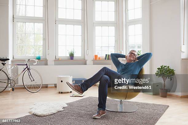 relaxed mature man at home sitting in chair - hands behind head stock pictures, royalty-free photos & images