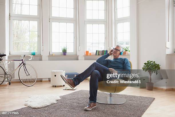 relaxed mature man at home sitting in chair listening to music - headphones eyes closed stock pictures, royalty-free photos & images