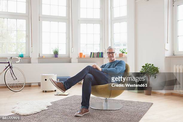 relaxed mature man at home sitting in chair - mann sitzt auf stuhl stock-fotos und bilder
