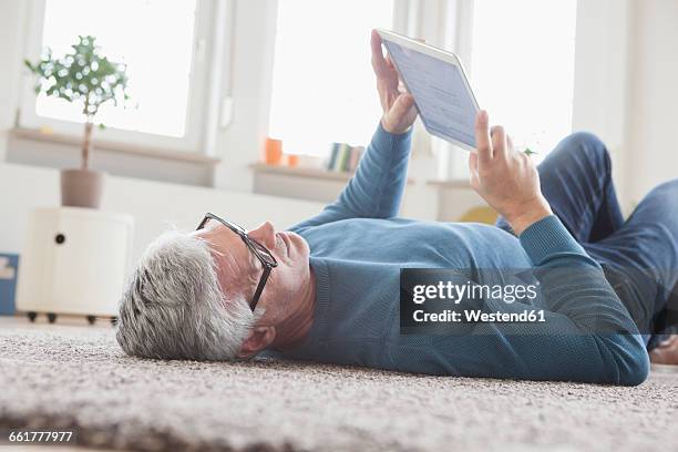 mature man at home lying on floor using digital tablet - reclining stock pictures, royalty-free photos & images