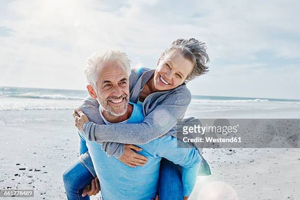 man giving his wife a piggyback ride on the beach - 50 59 years stock pictures, royalty-free photos & images