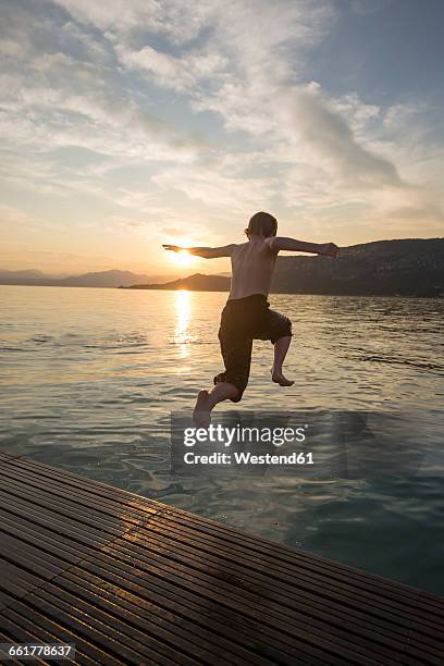 italy, veneto, bardolino, lake garda, boy jumping into the water at sunset - bathing in sunset stock pictures, royalty-free photos & images