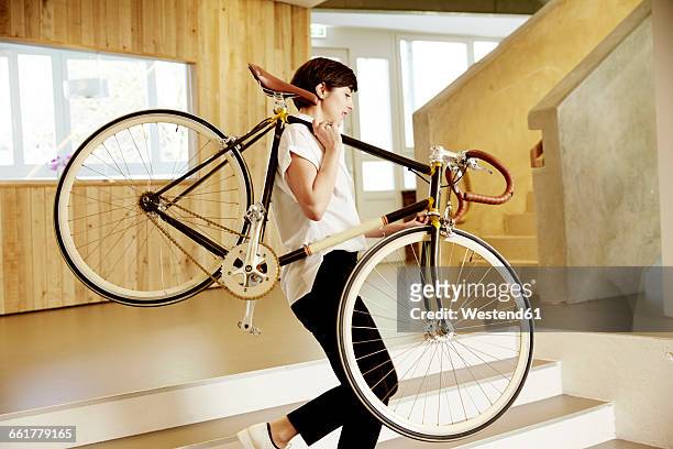 woman carrying racing cycle on her shoulder in an office - walking with bike stock-fotos und bilder