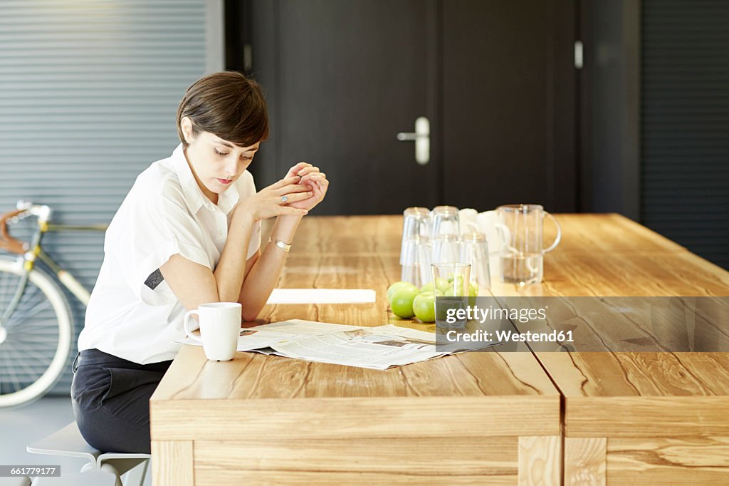 Woman reading newspaper at wooden table in a modern canteen