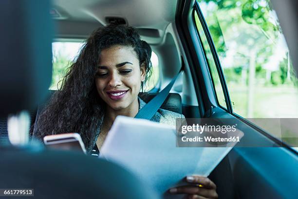 smiling young woman in car with folder and cell phone - sitting in car stock pictures, royalty-free photos & images