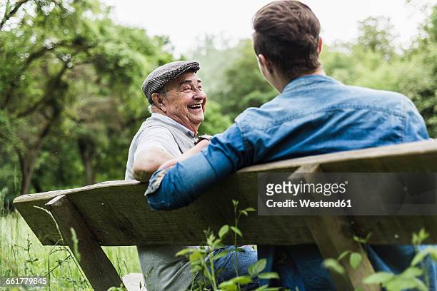 laughing senior man sitting on a bench with his grandson - senior men talking stock pictures, royalty-free photos & images