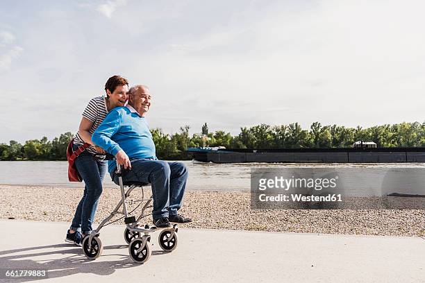 woman pushing her old father sitting on wheeled walker - father and grown up daughter stock-fotos und bilder