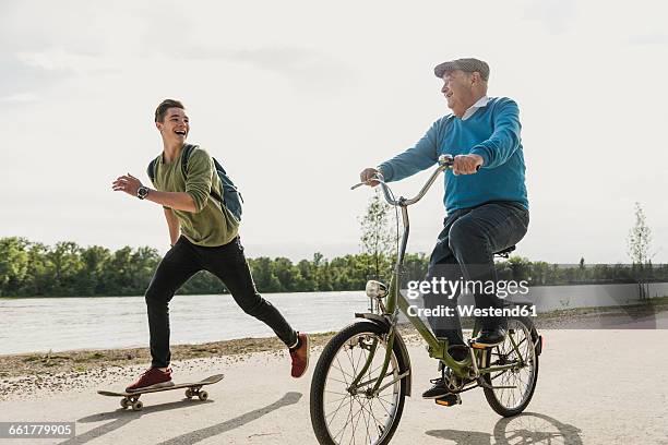 grandfather and grandson having fun together at riverside - old man bicycle stock-fotos und bilder