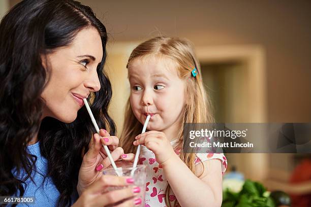 mother and daughter face to face drinking smoothie with straws - drinking straw stock-fotos und bilder