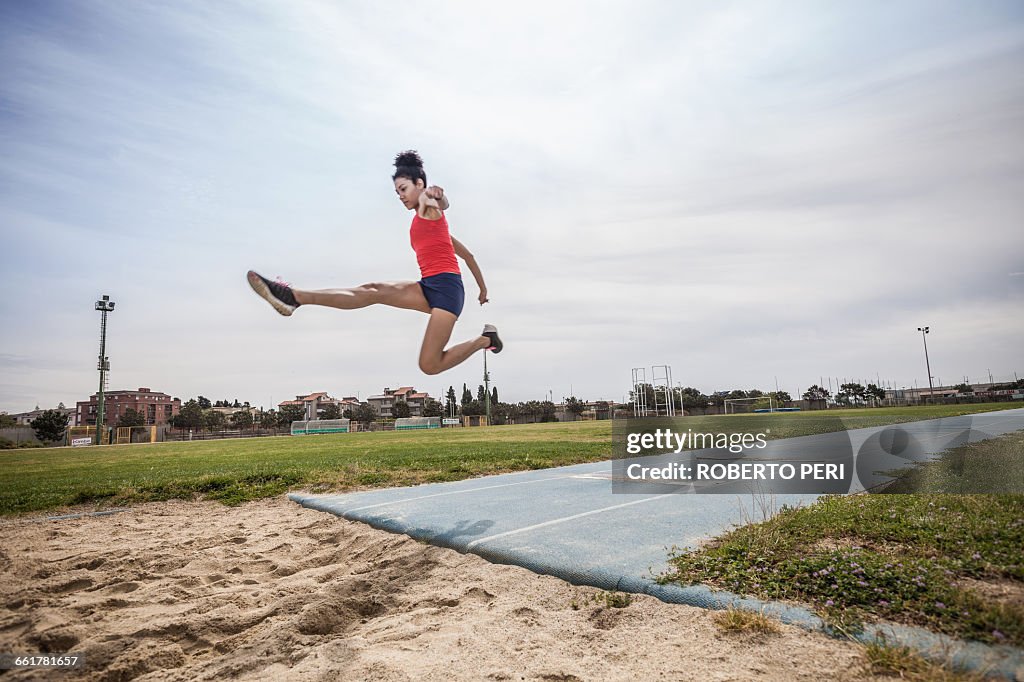 Young female long jumper jumping mid air at sport facility