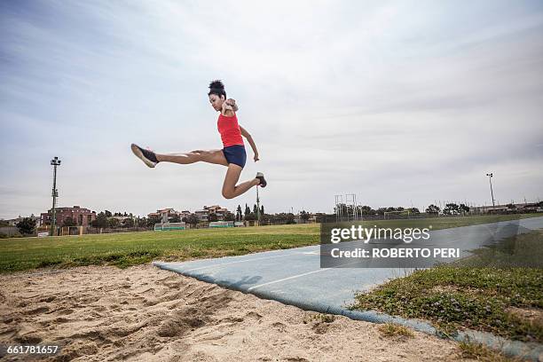 young female long jumper jumping mid air at sport facility - salto em comprimento imagens e fotografias de stock