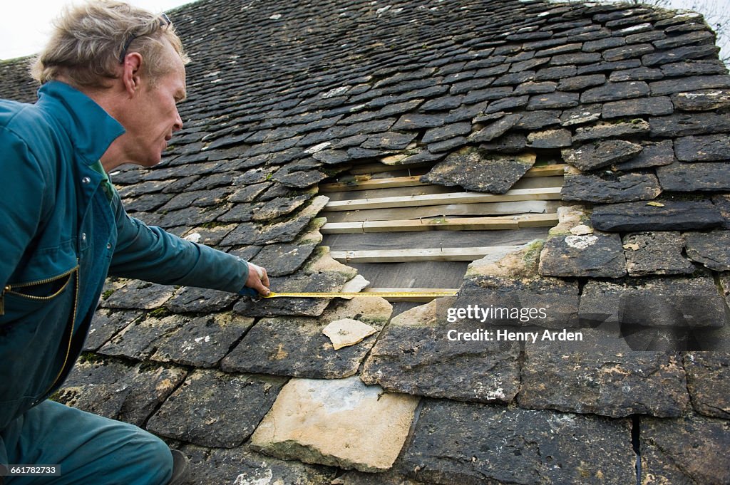 Roofer measuring hole in traditional stone tile roof