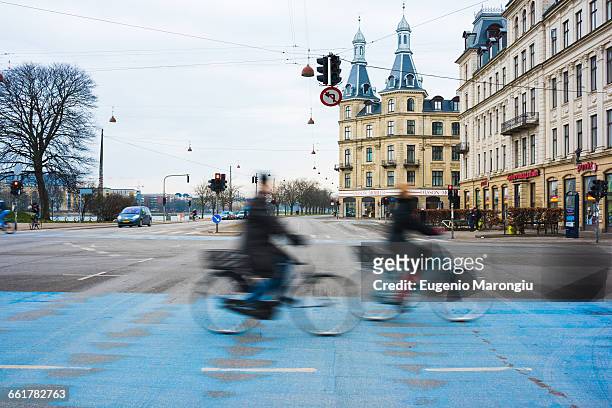 two cyclists speeding along blue city cycle path, copenhagen, denmark - denmark cycling stock pictures, royalty-free photos & images