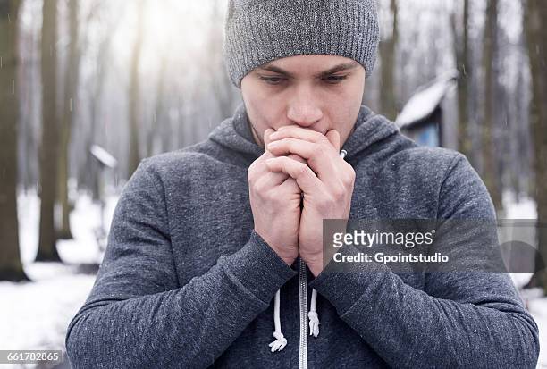 young man breathing on hands, in snowy forest - exhale stock pictures, royalty-free photos & images