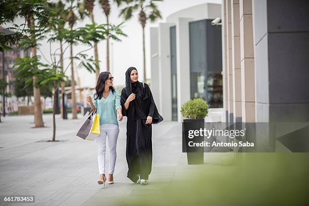 young middle eastern woman wearing traditional clothing walking along street with female friend, dubai, united arab emirates - arab woman walking ストックフォトと画像