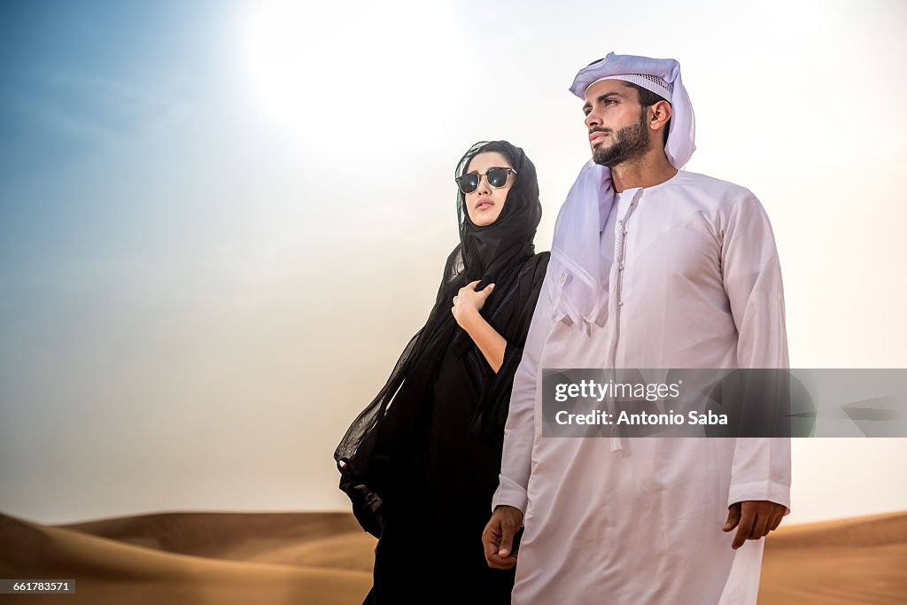 Couple wearing traditional middle eastern clothes in desert, Dubai, United Arab Emirates