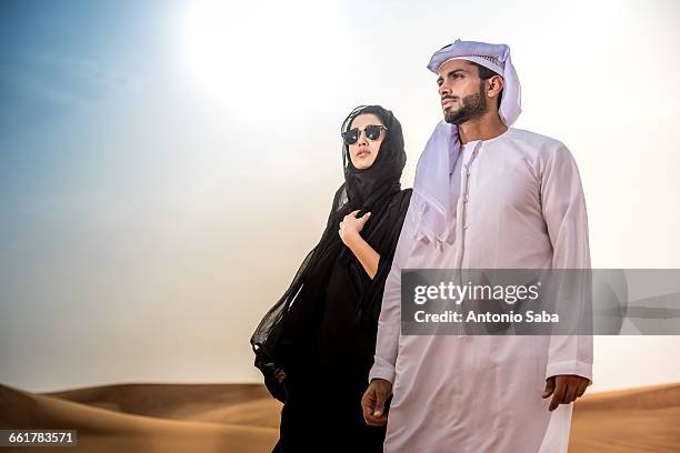 couple wearing traditional middle eastern clothes in desert, dubai, united arab emirates - uae heritage stock pictures, royalty-free photos & images