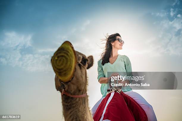 low angle view of female tourist riding camel in desert, dubai, united arab emirates - camel ride stock pictures, royalty-free photos & images