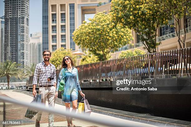 couple strolling on walkway carrying shopping bags, dubai, united arab emirates - dubai tourist stock pictures, royalty-free photos & images