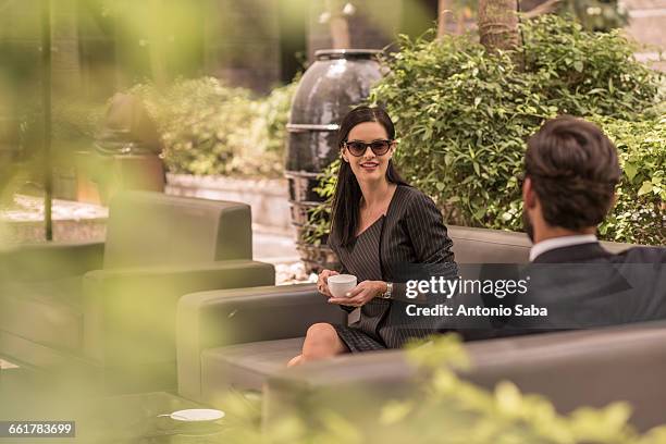 businessman and woman talking on hotel garden sofa, dubai, united arab emirates - ドバイ　ホテル ストックフォトと画像