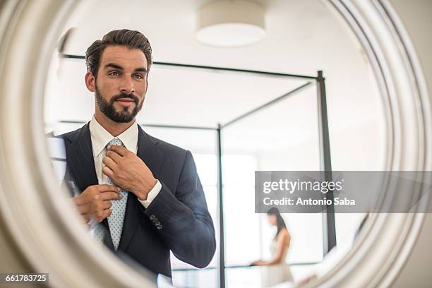 mirror reflection of young businessman adjusting shirt and tie in hotel room, dubai, united arab emirates - eitelkeit stock-fotos und bilder
