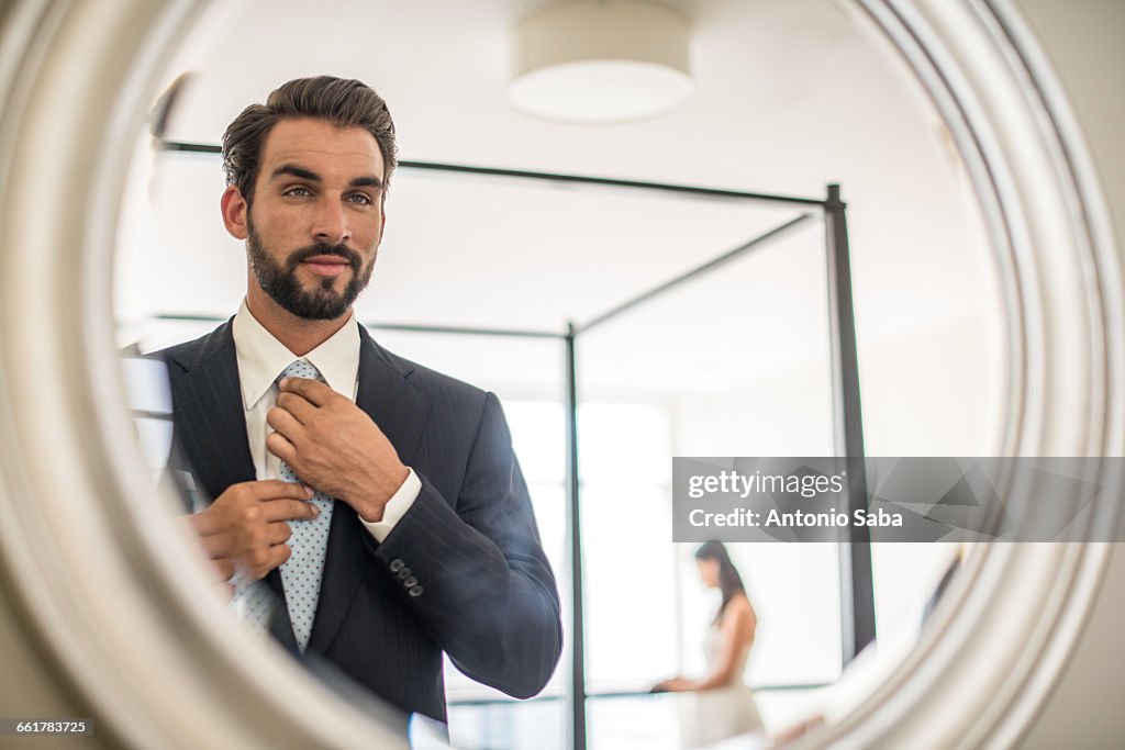 Mirror reflection of young businessman adjusting shirt and tie in hotel room, Dubai, United Arab Emirates