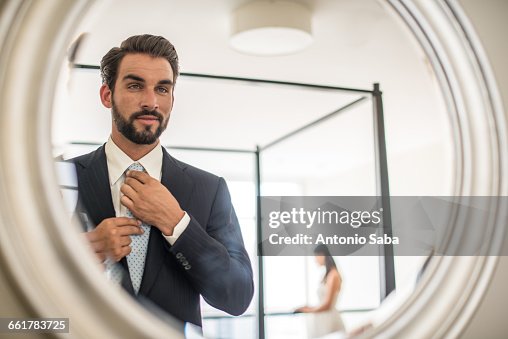 Mirror reflection of young businessman adjusting shirt and tie in hotel room, Dubai, United Arab Emirates Mirror reflection of young businessman adjusting shirt and tie in hotel room, Dubai, United Arab Emirates