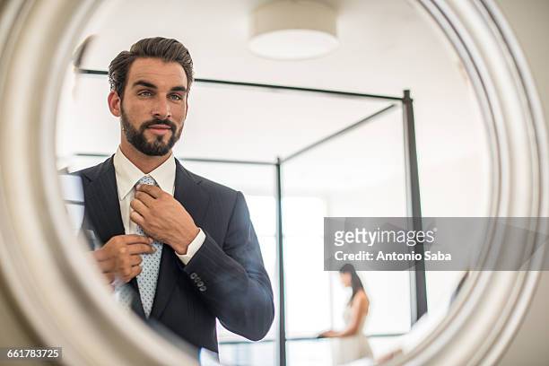 mirror reflection of young businessman adjusting shirt and tie in hotel room, dubai, united arab emirates - vanity stock pictures, royalty-free photos & images