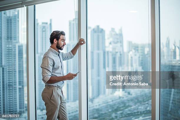 businessman with smartphone staring through window with skyscraper view, dubai, united arab emirates - dubai skyline stock pictures, royalty-free photos & images