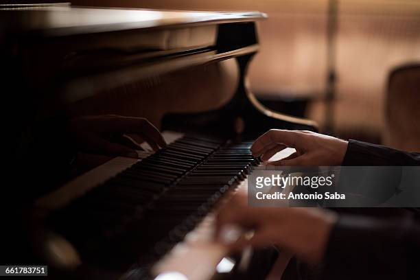 hands of young man playing piano keys in bar at night - klavier stock-fotos und bilder