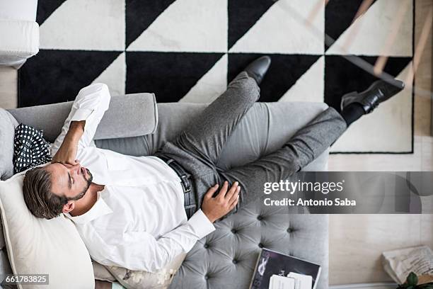 overhead view of young businessman reclining asleep on hotel room chaise longue, dubai, united arab emirates - diva papel humano - fotografias e filmes do acervo