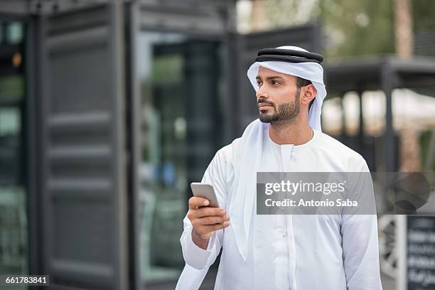 man wearing traditional middle eastern clothing using smartphone, dubai, united arab emirates - emirati arabi uniti foto e immagini stock
