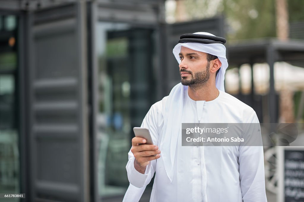 Man wearing traditional middle eastern clothing using smartphone, Dubai, United Arab Emirates