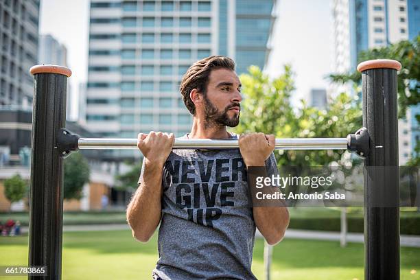 young man doing pull ups on park exercise equipment, dubai, united arab emirates - chin ups stock pictures, royalty-free photos & images