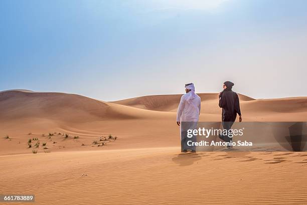 couple wearing traditional middle eastern clothes walking in desert, dubai, united arab emirates - united arab emirates stock-fotos und bilder