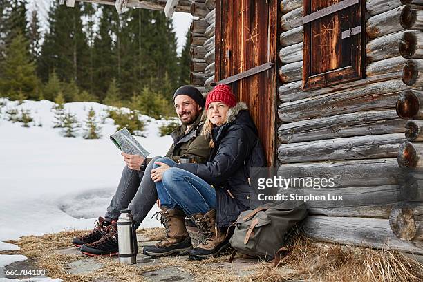 portrait of couple reading map sitting outside log cabin in winter, elmau, bavaria, germany - bayern winter stock-fotos und bilder