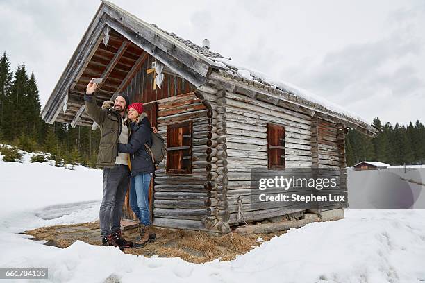 couple taking smartphone selfie outside log cabin in winter, elmau, bavaria, germany - traditional parka stock pictures, royalty-free photos & images