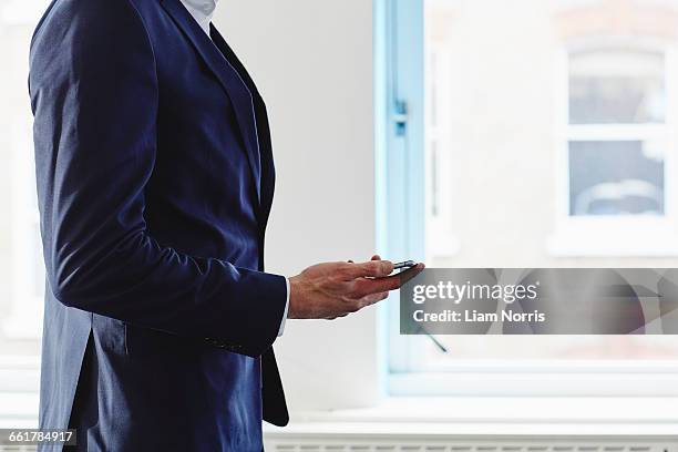 cropped side view of man wearing suit holding smartphone - world at your fingertips engelse uitdrukking stockfoto's en -beelden